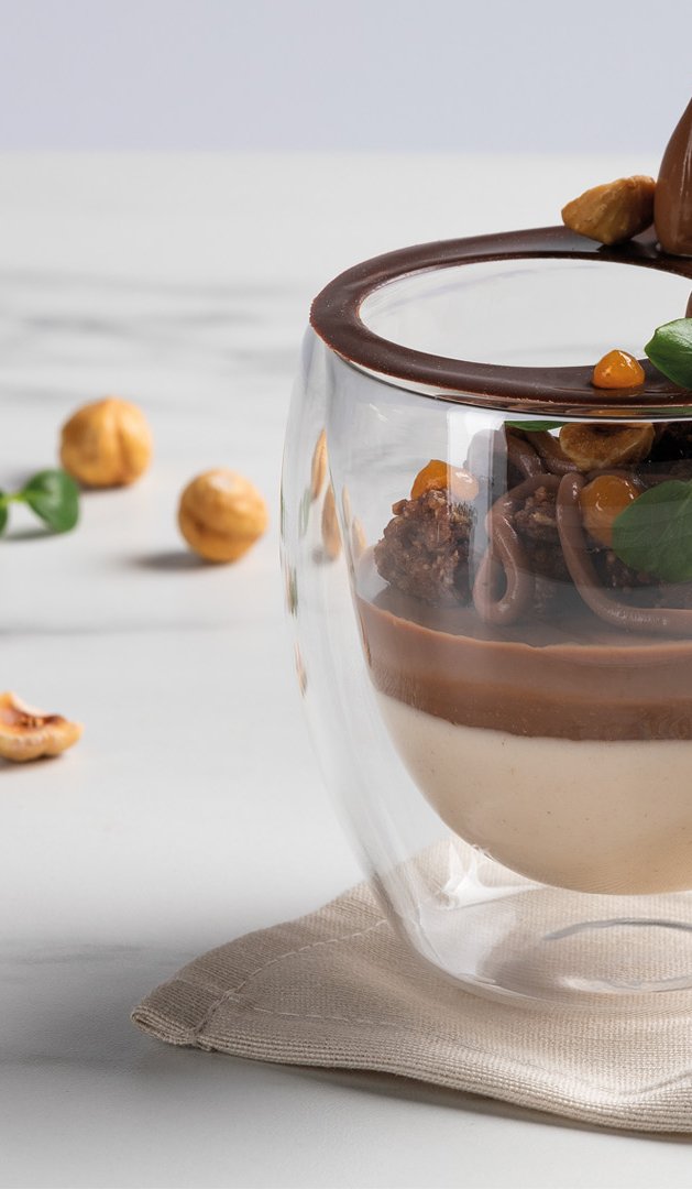 Dessert en verrine, mousse chocolat et caramel en couches, garni de noisettes et menthe sur marbre.