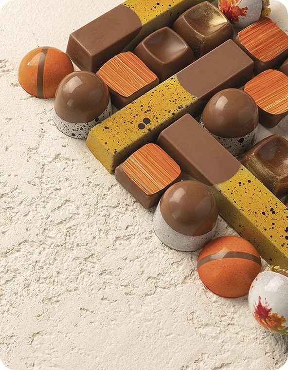 Assortiment de chocolats gourmets en formes carrées et dômes, finitions marron, mouchetées d'or et marbrées orange