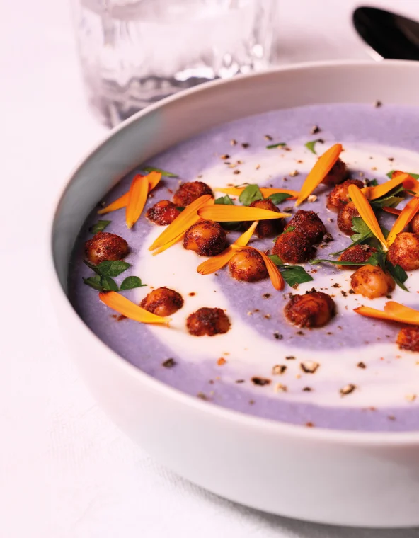 Bol blanc de soupe violette virevoltée de crème, pois chiches épicés, herbes et fleurs d'oranger.