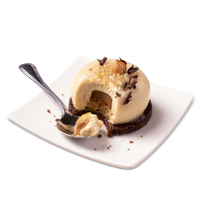 Dessert dôme mousse au caramel sur base biscuit chocolat, garni de noisettes et copeaux de chocolat, avec une bouchée...