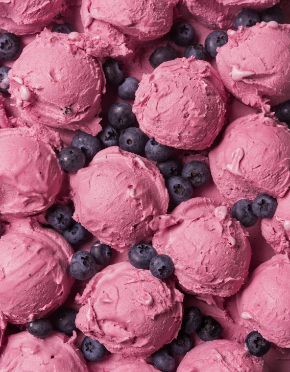 Gros plan de boules de glace rose avec des myrtilles fraîches éparpillées, remplissant tout le cadre.