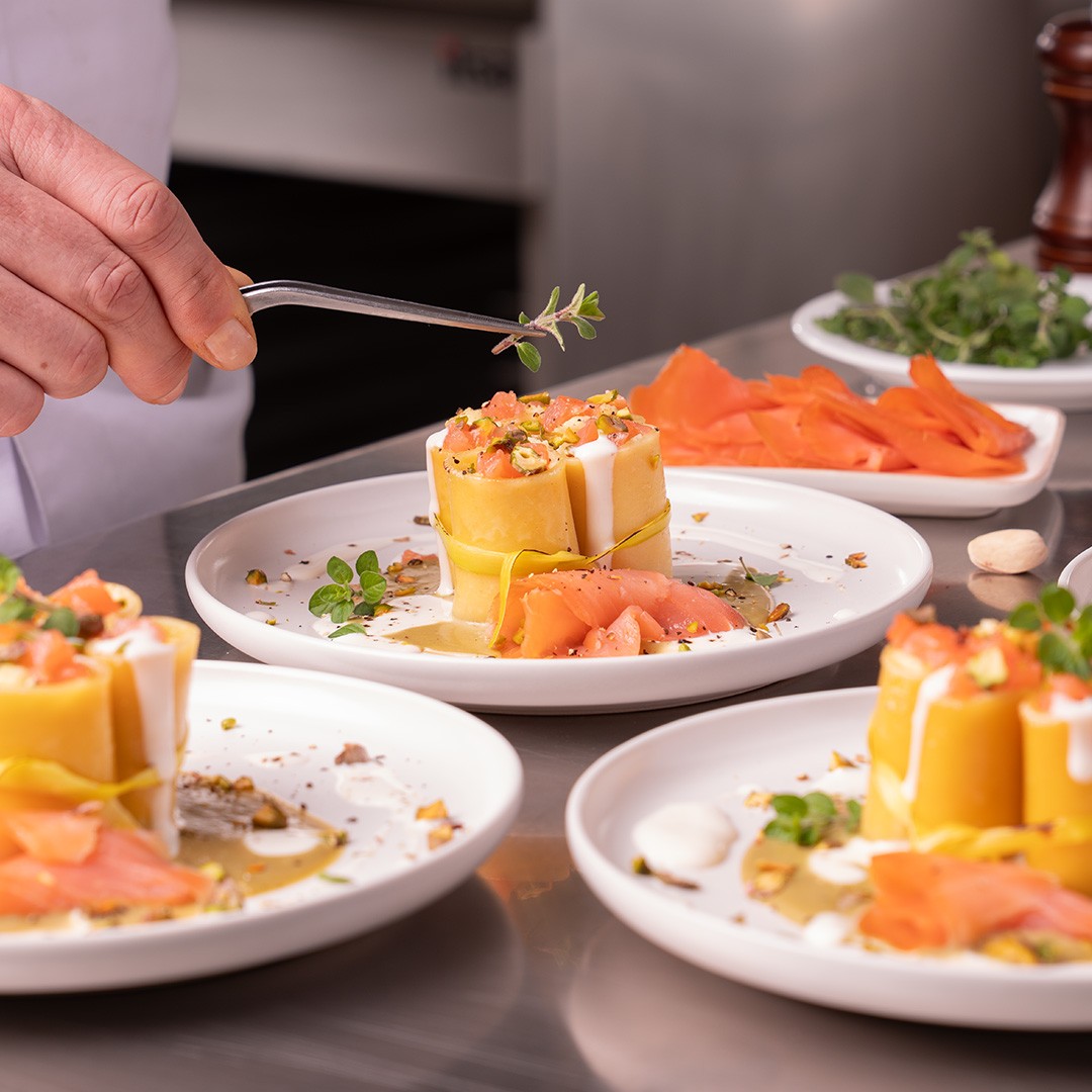 Chef utilisant une pince pour dresser des rouleaux de pâtes avec saumon fumé, pistaches et herbes