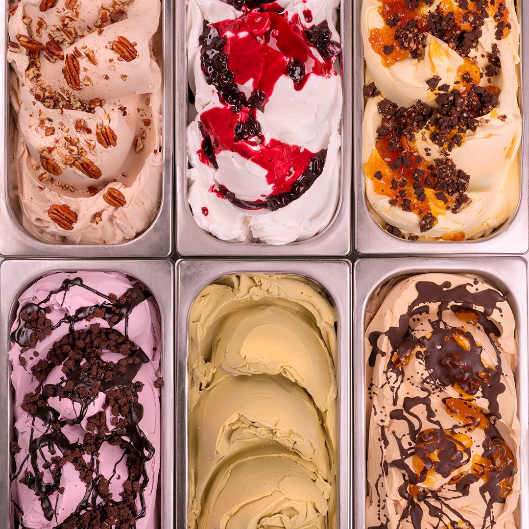 Six bacs métalliques de gelato aux saveurs variées, dont noix de pécan, fruits rouges, pistache et chocolat-caramel, ...