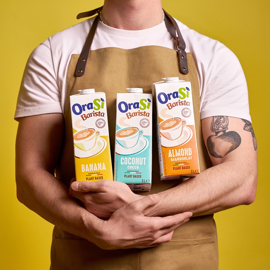 Une personne en tablier beige tient trois briques de lait végétal OraSì Barista : banane, noix de coco et amande