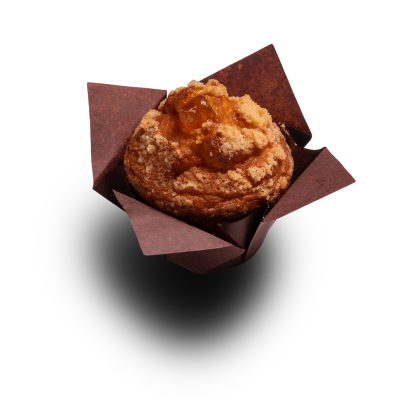Muffin doré garni de streusel et de fourrage aux fruits, dans une caissette en papier brun, fond blanc.