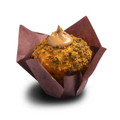 Muffin enrobé de pistaches concassées, garni d'un tourbillon de glaçage caramel, dans une caissette tulipe marron.