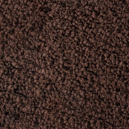 Gros plan d'une surface brun foncé et friable, rappelant une terre grossière ou du marc de café.