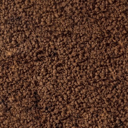 Gros plan de terre friable brune ou de marc de café à la texture grossière et granuleuse remplissant le cadre.