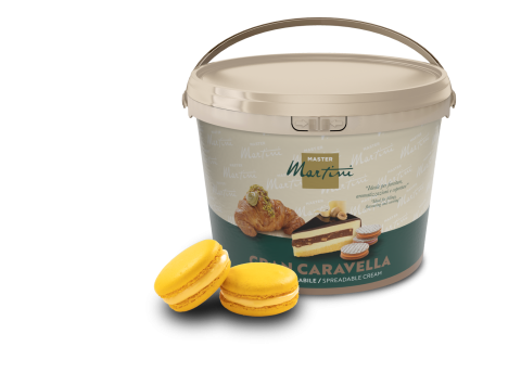 Seau beige de crème à tartiner Master Martini Gran Caravella à côté de deux macarons jaunes et d'une pâtisserie fourrée.