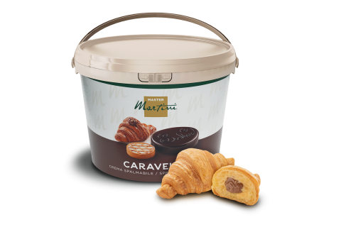 Seau beige de crème chocolatée à tartiner Master Martini Caravel près de deux croissants, un fourré au chocolat.