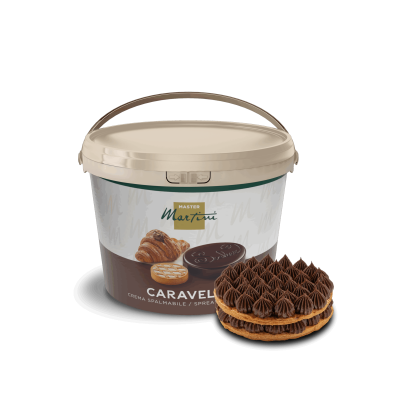 Un seau de crème tartinable au chocolat Master Martini Caravella à côté d'une pâtisserie décorée de volutes de chocolat.