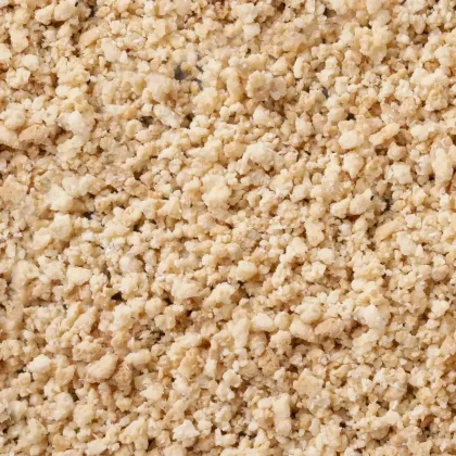 Gros plan sur des granules beige clair friables, à texture grossière type crumble, couvrant tout le cadre