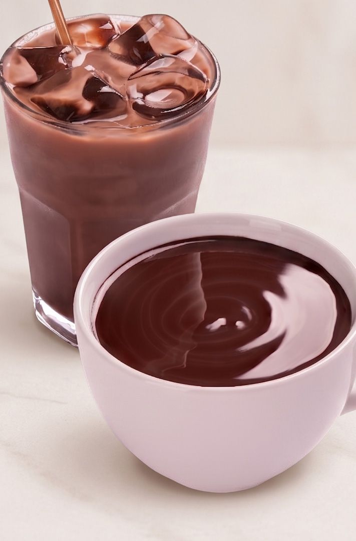 Verre de chocolat glacé avec paille à côté d'une tasse rose de chocolat chaud sur du marbre