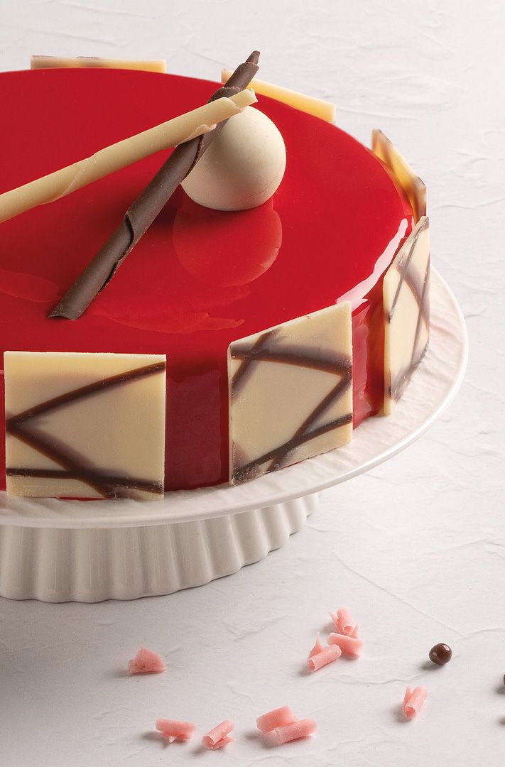 Gâteau rond glaçage miroir rouge brillant, plaques de chocolat blanc et bâtonnet de chocolat