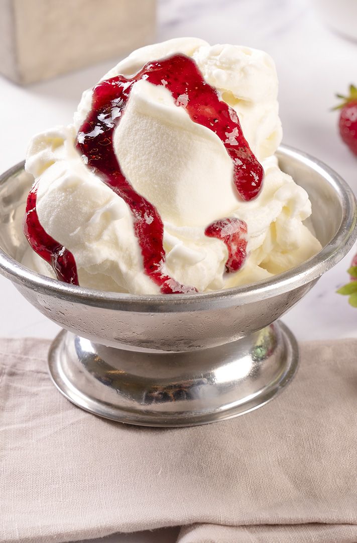 Glace vanille nappée de coulis de fraise dans un récipient métallique, entourée de fraises fraîches sur serviette beige