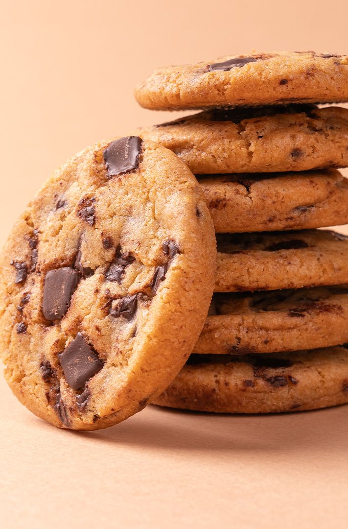 Pile de cookies aux pépites de chocolat, l'un appuyé contre le tas, fond pêche