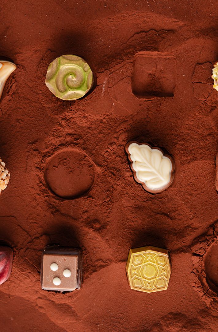 Chocolats décoratifs variés avec motifs peints et enrobage de fruits secs, disposés sur cacao en poudre