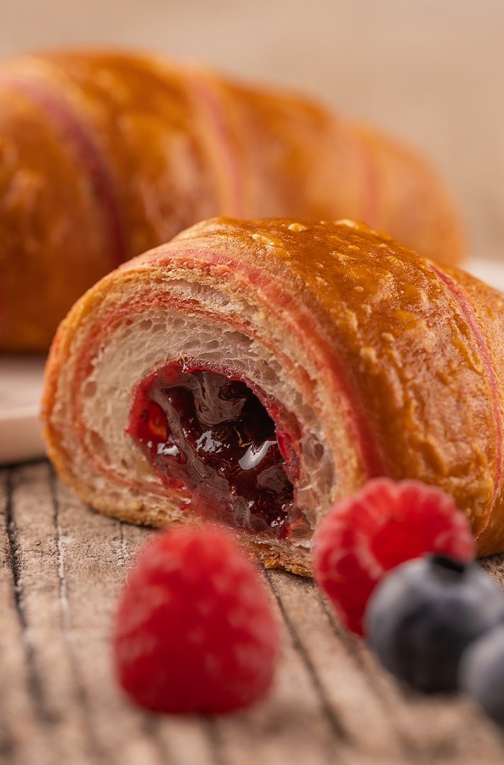 Croissant doré aux rayures rouges coupé révélant une garniture de confiture de baies, entouré de framboises et myrtilles