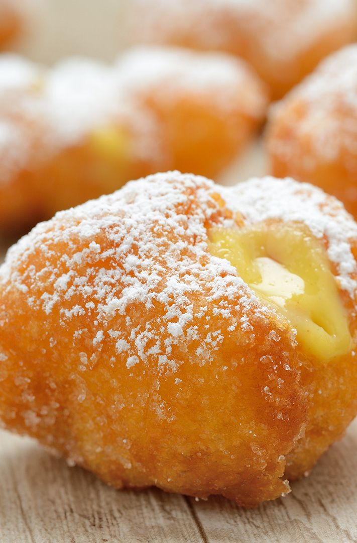 Beignet frit saupoudré de sucre glace, fourré à la crème, sur bois avec d'autres beignets flous en arrière-plan