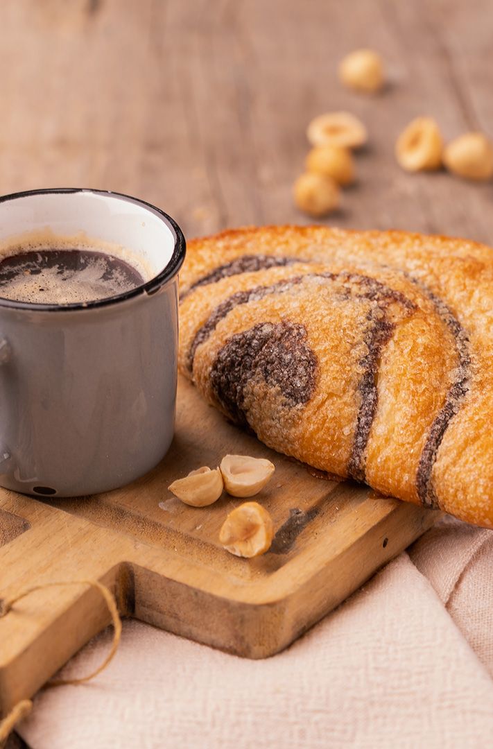 Viennoiserie tourbillon au chocolat avec un café noir, noisettes décortiquées et un linge en lin sur planche en bois