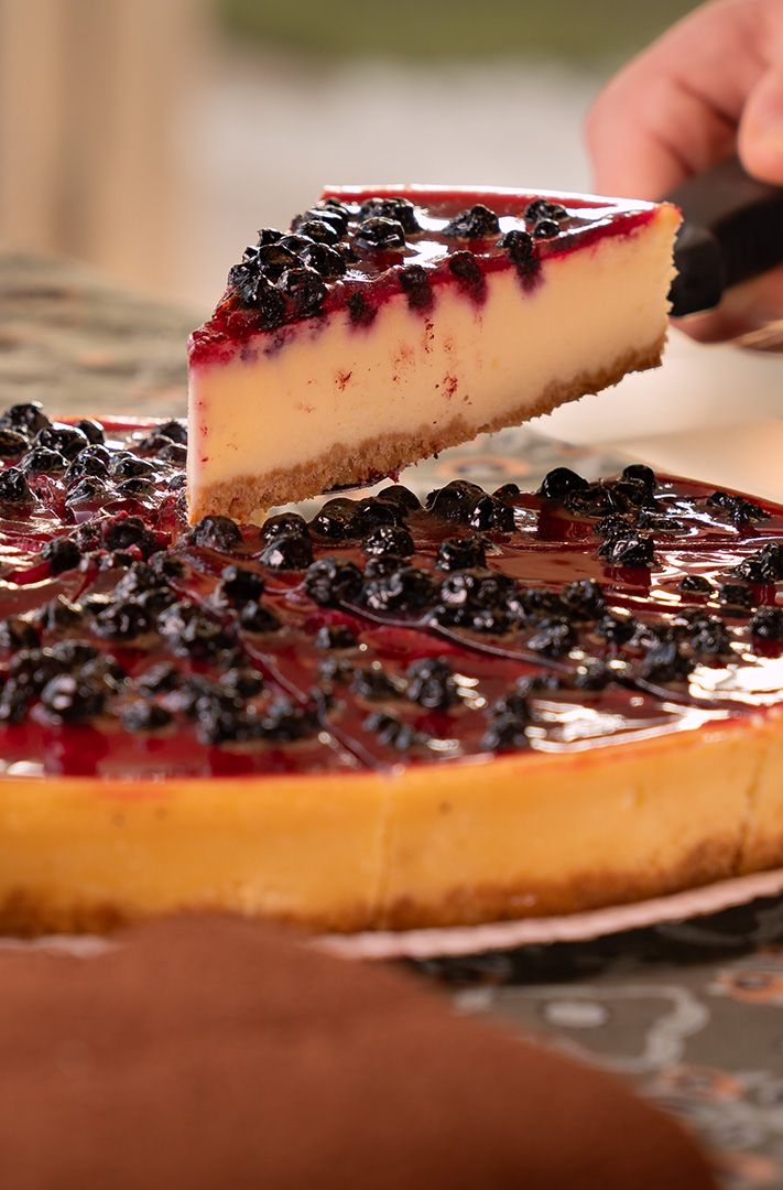 Cheesecake entier aux myrtilles nappé d'un glaçage rouge brillant, avec une part prélevée à la pelle à gâteau