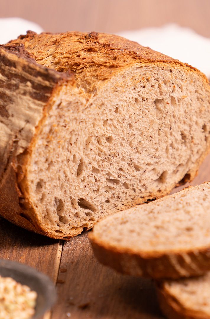 Pain complet tranché à croûte croustillante et mie aérée, sur table en bois avec des grains à proximité.