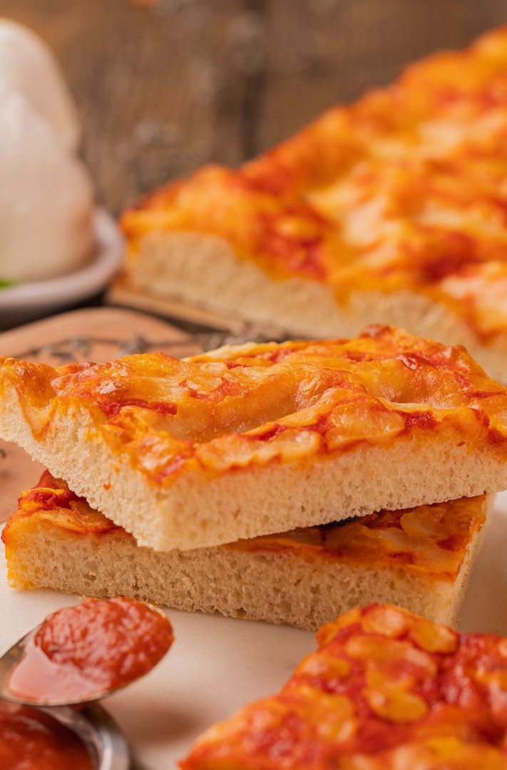 Tranches carrées de pizza focaccia à la tomate et au fromage empilées près de sauce marinara, mozzarella fraîche et h...