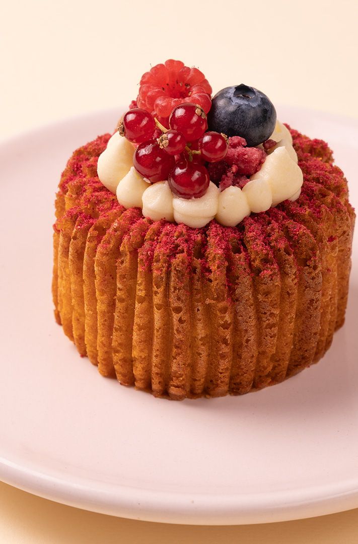 Petit gâteau strié saupoudré de poudre rouge, garni de crème fouettée, groseilles rouges, framboise et myrtille
