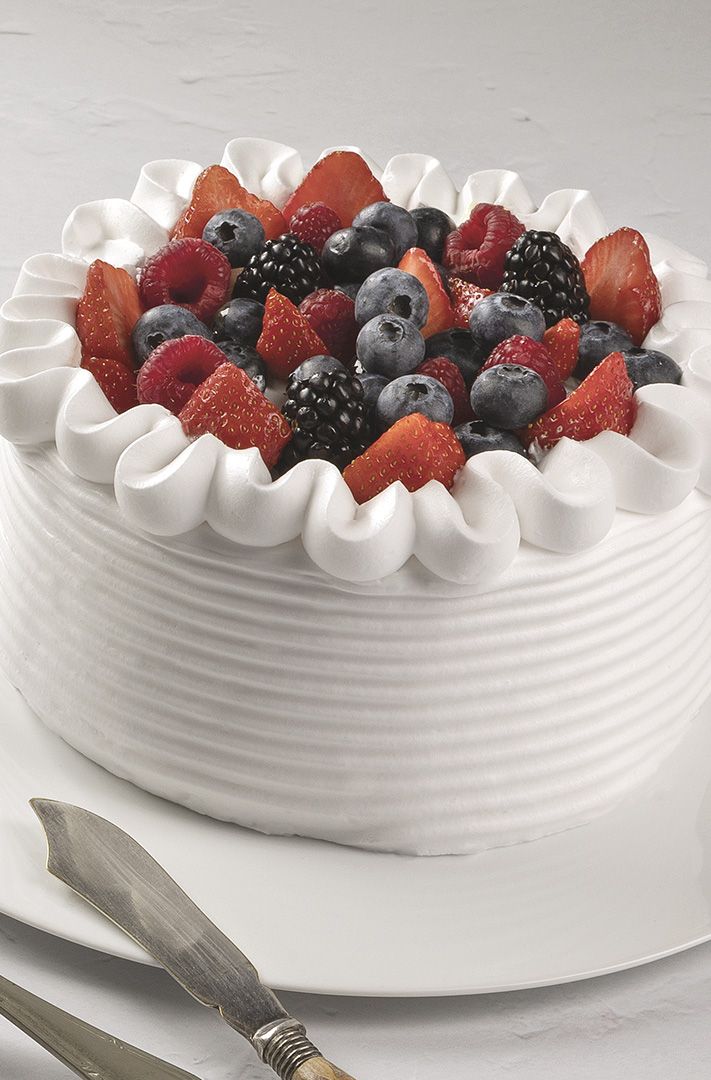 Gâteau rond glacé blanc aux bords striés, garni de fraises, myrtilles, framboises et mûres fraîches.