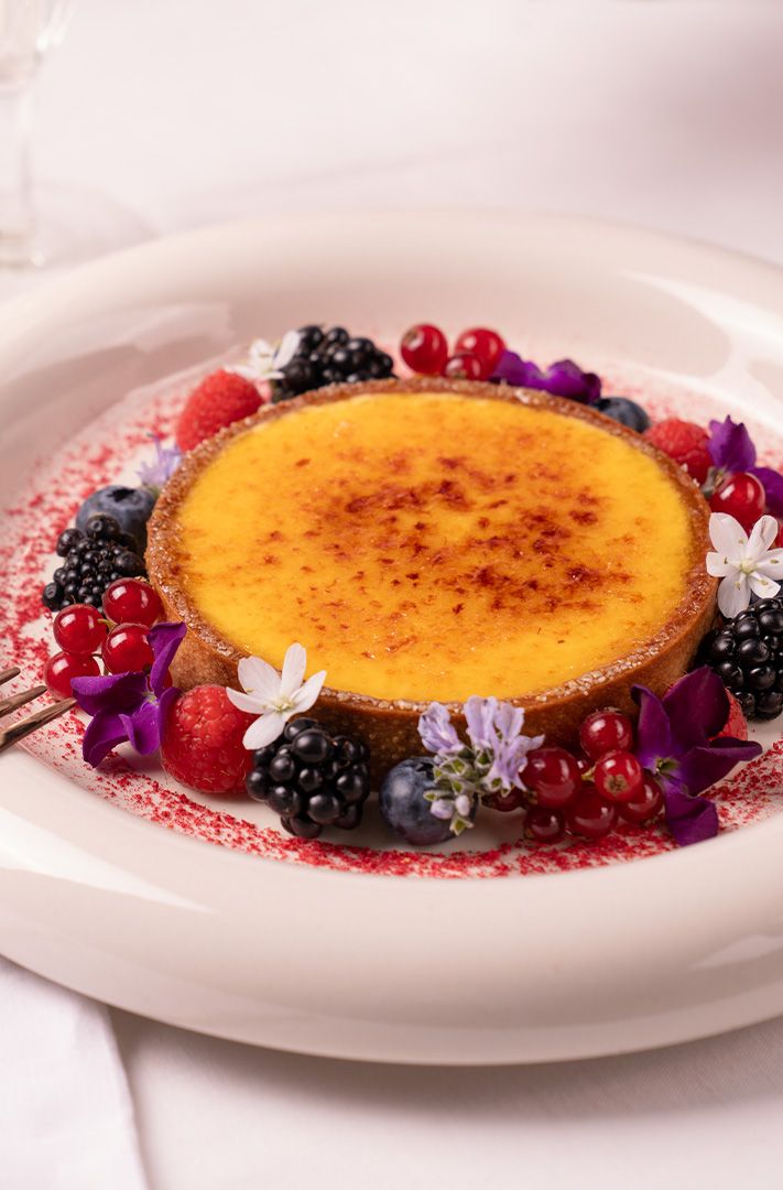 Tarte à la crème caramélisée garnie de mûres, framboises, myrtilles, groseilles rouges et fleurs comestibles