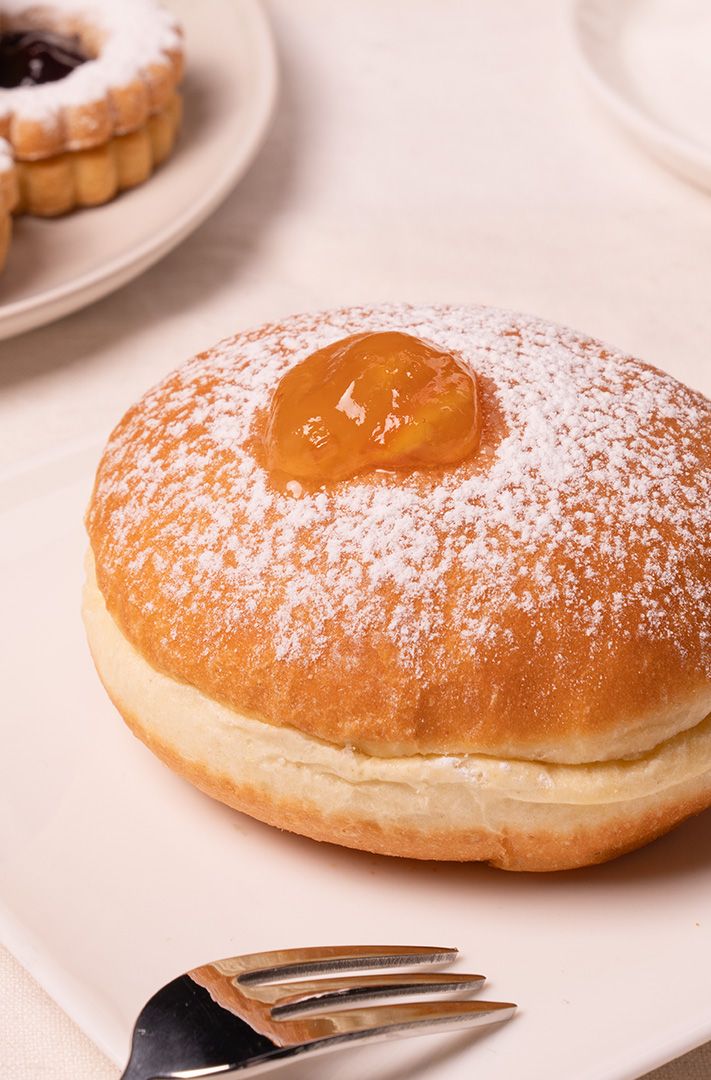 Beignet fourré à la confiture saupoudré de sucre glace sur assiette blanche, avec fourchette et sablés à la confiture...