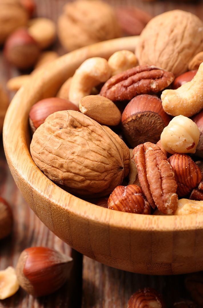 Bol en bois rempli de fruits secs variés : noix, noix de pécan, noisettes et noix de cajou entières