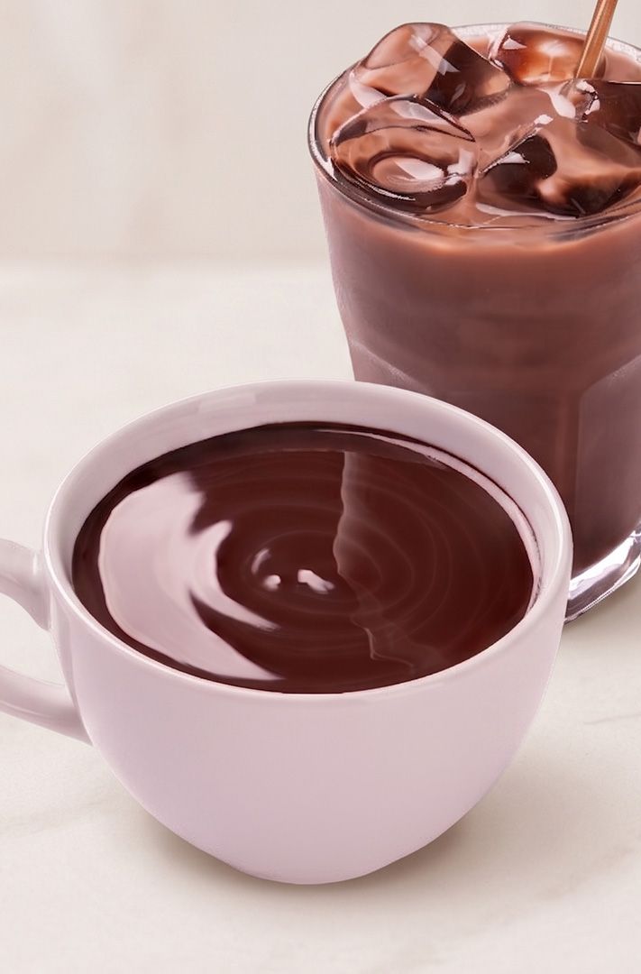 Mug rose de chocolat chaud à côté d'un verre de chocolat glacé avec paille, sur marbre blanc.