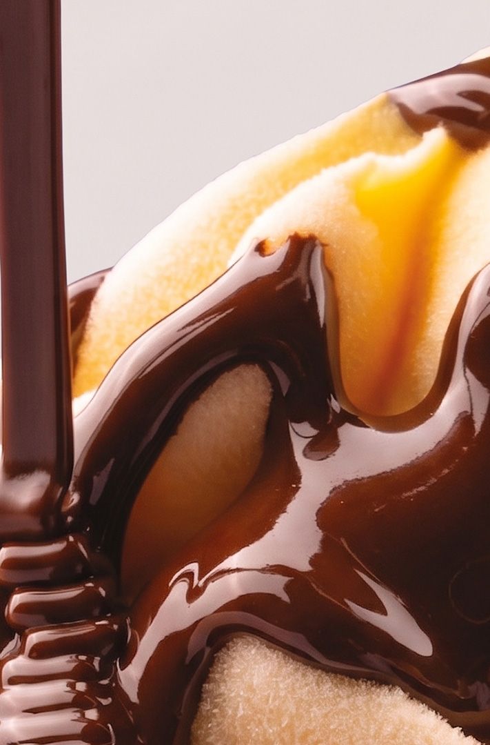 Gros plan sur du sirop de chocolat brillant versé sur une glace à la vanille, formant des filets et volutes.