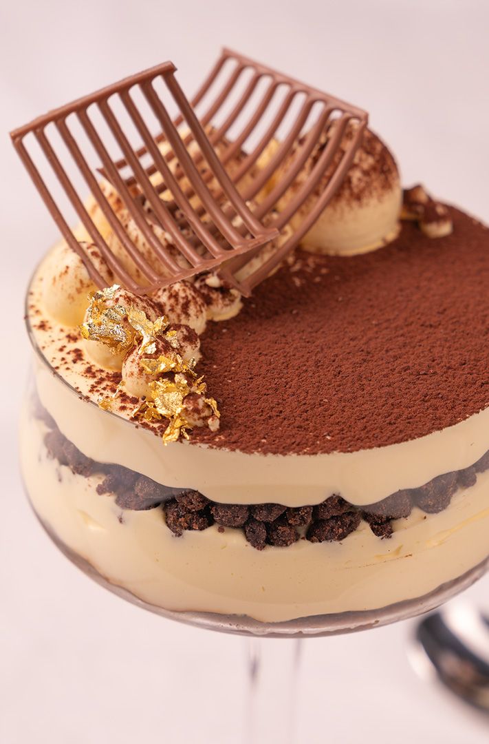 Tiramisu en couches servi dans un verre, saupoudré de cacao, feuilles d'or et décor en résille de chocolat