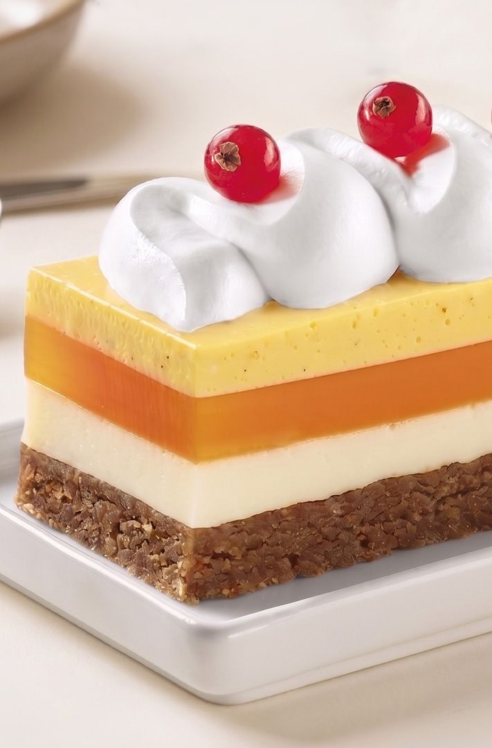 Dessert rectangulaire en couches avec base de crumble, crème blanche, couches de gelée orange et jaune, garni de crèm...