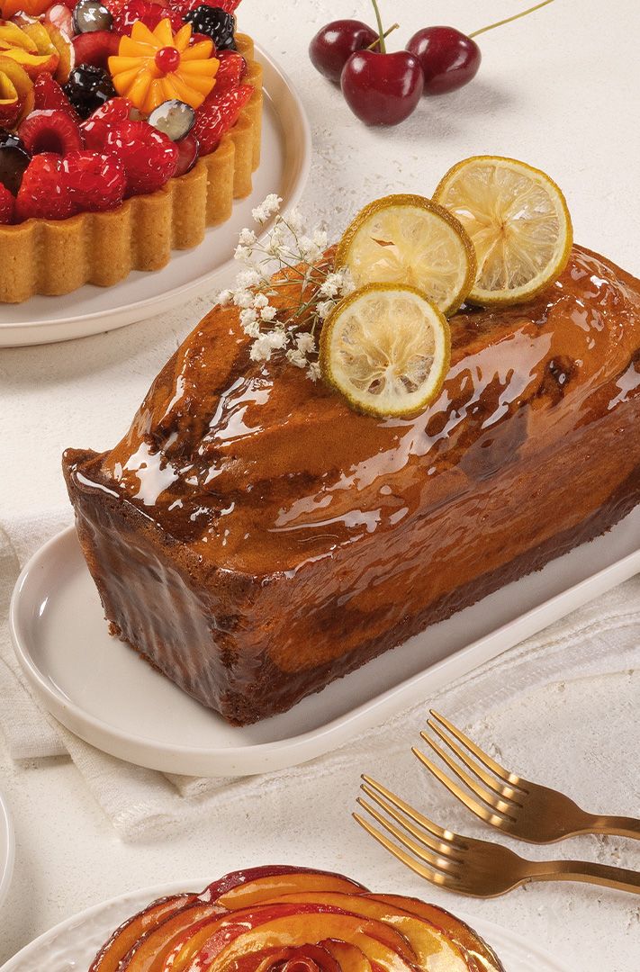 Cake aux agrumes glacé avec tranches de citron confit, à côté d'une tarte aux fruits, cerises et fourchettes dorées s...