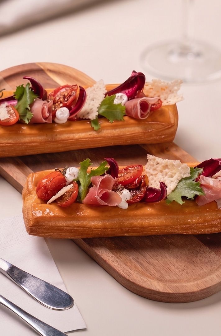 Deux tartelettes en pâte feuilletée garnies de prosciutto, tomates cerises, mozzarella, radicchio et tuiles de fromag...