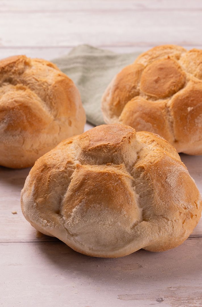 Trois petits pains kaiser dorés à la croûte farinée en pétales, sur bois blanc et tissu vert sauge