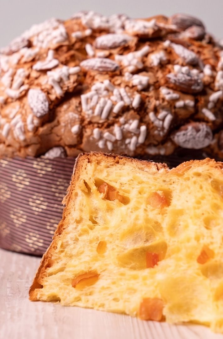 Panettone entier avec croûte aux amandes et sucre, tranche coupée montrant l'intérieur moelleux aux fruits confits