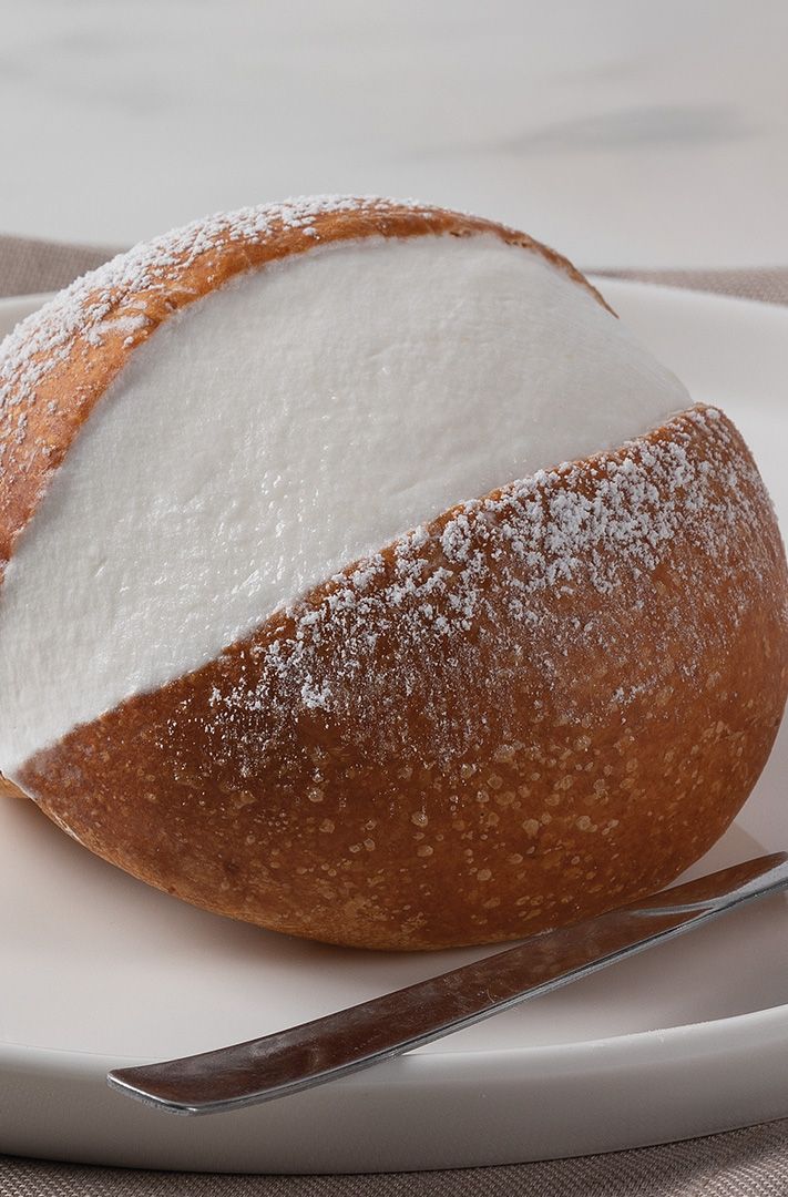 Petit pain rond croustillant saupoudré de sucre glace, tranché sur assiette blanche avec fourchette