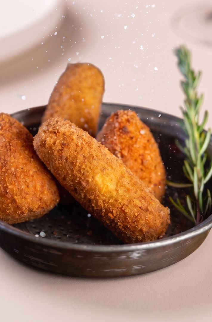 Quatre croquettes panées dorées dans une petite poêle en métal, garnies de romarin et d'une pincée de sel.