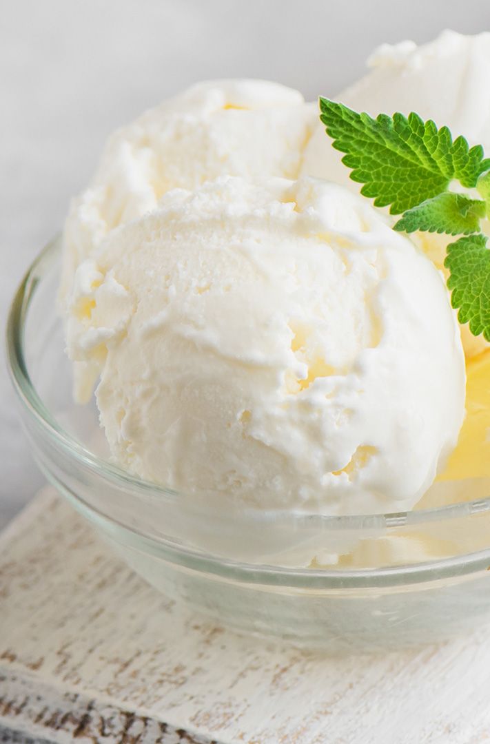 Deux boules de glace vanille dans un bol en verre, garnies de menthe fraîche sur une planche en bois blanc.